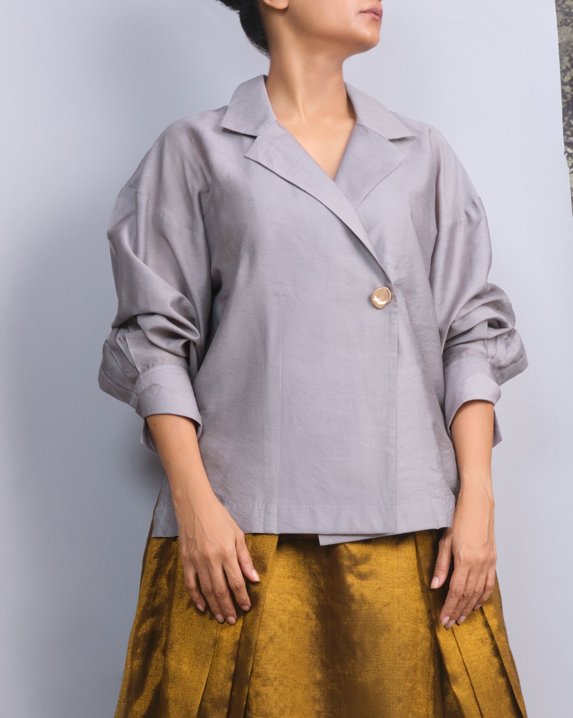 Woman wearing a light gray blouse and mustard yellow skirt against a neutral background