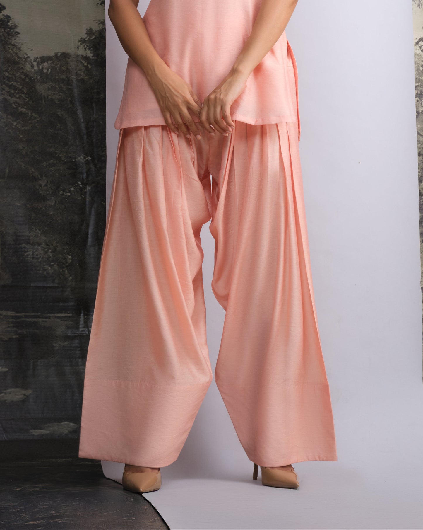 Woman wearing a pink sleeveless top and wide-leg pants against a white background