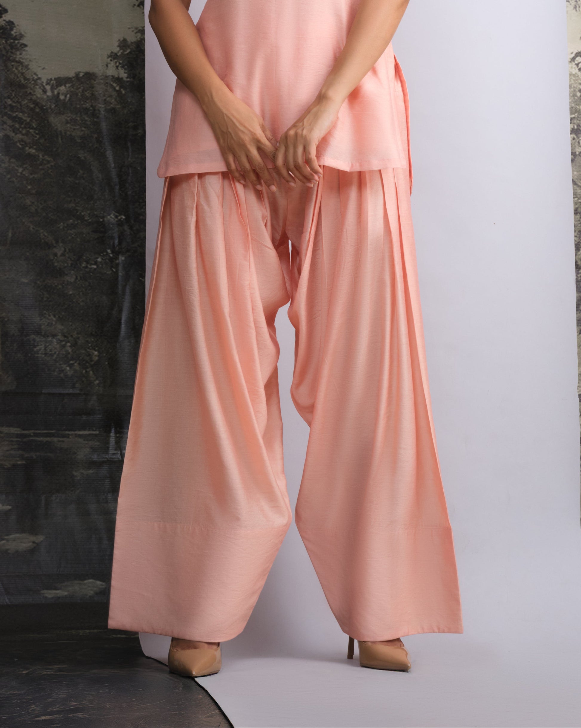 Woman wearing a pink sleeveless top and wide-leg pants against a white background