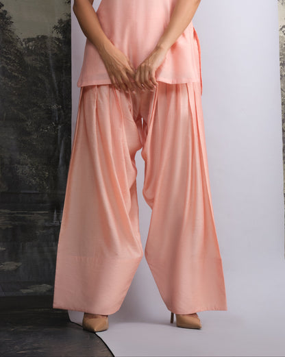 Woman wearing a pink sleeveless top and wide-leg pants against a white background