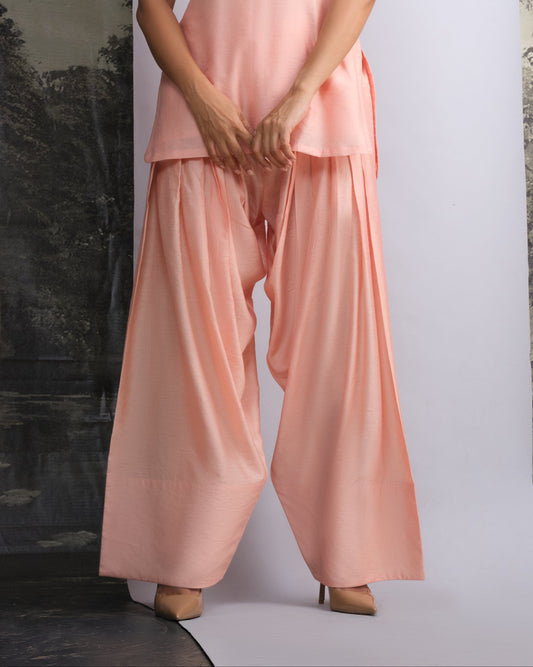 Woman wearing a pink sleeveless top and wide-leg pants against a white background